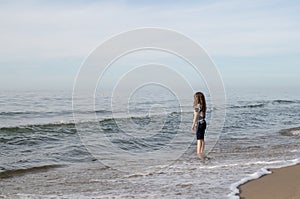 One long-haired girl running along the shore of the silver-colored North sea. Windy weather, Northern landscape, pastel color
