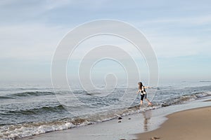 One long-haired girl running along the shore of the silver-colored North sea. Windy weather, Northern landscape, pastel color
