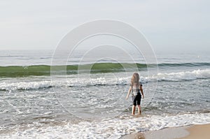 One long-haired girl running along the shore of the silver-colored North sea. Windy weather, Northern landscape, pastel color