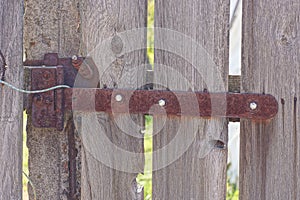 One long rusty brown door hinge on gray wooden fence