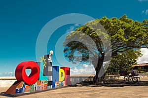 Sign of the city of Olinda next to a tree, in Alto da SÃ©, with the city of Recife in the background - Inst