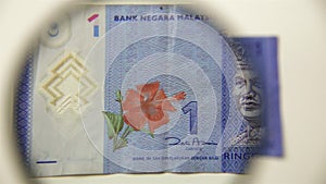 One Malaysian ringgit and magnifying glass.