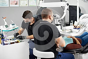 One male dentist is fixing a patient`s teeth while another male dentist is preparing the dental filling