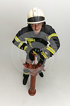 One male firefighter dressed in uniform standing at fire hydrant over white studio background.