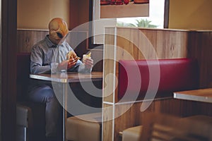 One man with alien mask eating alone inside a fast food store bad food hamburger and french fries. Ufo are among us living as