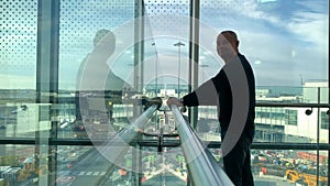 One man in a bright building of an airport lounge waiting at the window and looking at the street, travel concept