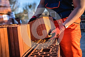 One man construction worker taking and carry or hold clay orange hollow blocks ar warehouse or construction site in sunny summer