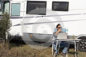 One man digital nomad lifestyle working on alternative outside workplace desk with a camper van motorhome house in background.