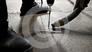 One man drills a hole in the floor with a hammer drill, the second holds a vacuum cleaner nearby. Floor repair, drilling