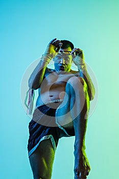 One man exercising thai boxing training on blue background in neon light.