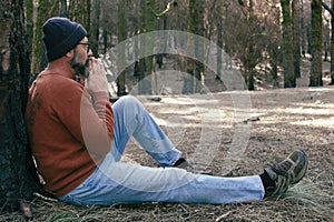 One man having relaxation time sitting on the ground in the middle of green forest woods and outdoor relax leisure activity.