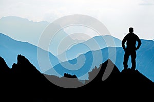 One Man reaching summit after climbing and hiking enjoying freedom and looking towards mountains silhouettes panorama