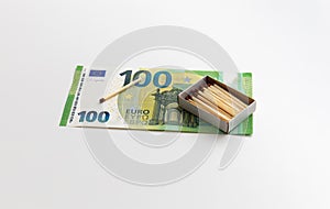 One matchstic and matches in box are on 100 euro banknotes, made of wood, production of matchsticks, white background