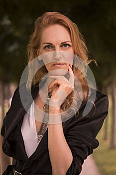 one mature Caucasian beautiful woman, late 40s, outdoors portrait upper body, hand on chin, looking at camera