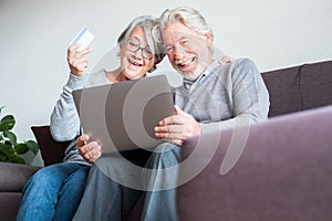 One mature couple of poeple on the sofa using her laptop and their credit card to buy something  - shopping online concept and