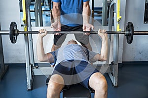 One mature man lying down on the bench of the gym training hus body to be fitness and active senior - man helping he holding de