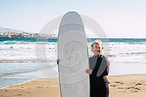 One mature woman with a surftable and wetsuit having fun at the beach smiling and having fun - senior learing surf and smiling