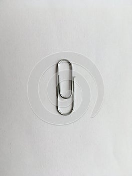 One metal paper clip lying on a white background. Abstraction.