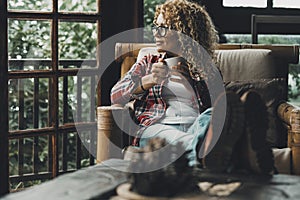 One middle age attractive woman relaxing at home sitting on the chair and looking outside enjoying afternoon time and indoor