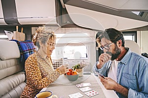 One middle age couple enjoy time playing cards together inside travel home camper van. People enjoying time on vacation smiling