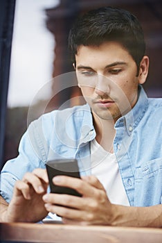 One mixed race handsome young man using his mobile phone while sitting outside in the city. Hispanic male texting and