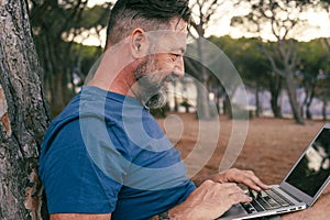 One modern adult man using and working on laptop at the park. Concept of smart working and freelance digital nomad small business