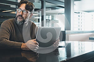 One modern man working on laptop at the desk in empty office or coworking space with light in background. Scared for security