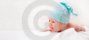 a one-month-old baby in a blue cap lies on his stomach and looks at the world. Family concept. Mockup on the header