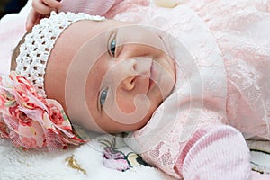 Beautiful newborn baby girl with a flower on her head smiling and looking at camera