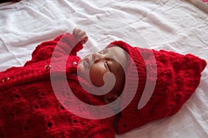 A one month old baby sleeping and swaddled in white cloth lying in white cloth background.