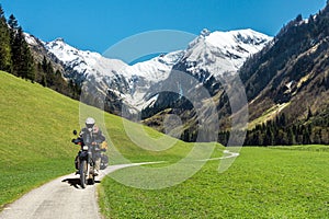 One motorbiker man driving on mountain valley road with snow covered mountains. Motorcycle adventure in the alps.