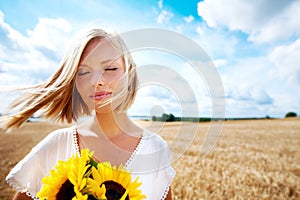 At one with nature. Happy young woman standing in a wheat field and holding some sunflowers.