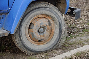 One old black big wheel in brown rust on a peanut truck is standing on the ground and grass