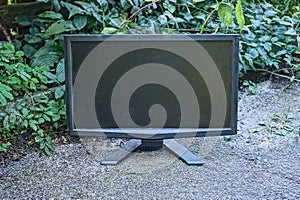 One old black computer monitor stands on gray asphalt