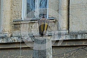 One old black iron lantern with yellow glass stands on a gray concrete pillar
