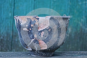 One old black large dirty broken ceramic pot with a crack