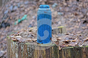 one old blue dirty plastic thermos stands on a gray wooden stump