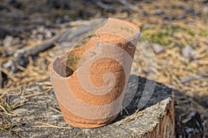 one old broken brown ceramic pot stands on a gray wooden stump