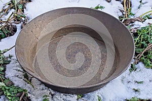 One old brown copper bowl stands on white snow