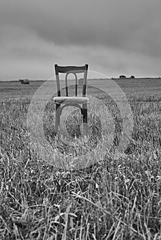 One old chair stands in a mown field against a cloudy sky