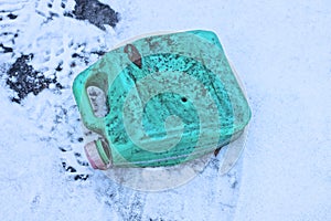 one old dirty green plastic canister lies on white snow
