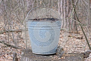 one old gray metal bucket stands on a wooden stump