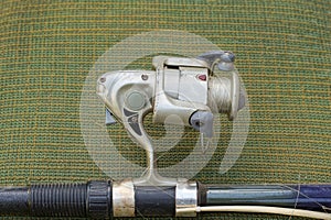One old gray metal spinning reel with a fishing line on a blue fishing rod