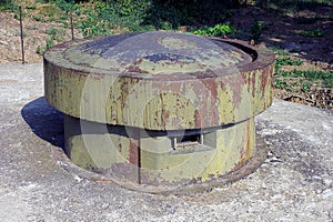 One old military green rusty iron tower with embrasures on a gray concrete pillbox
