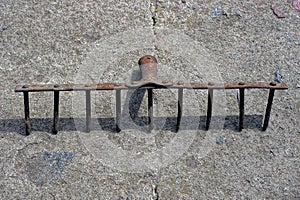 One old rusty brown iron rake lies on a gray stone floor
