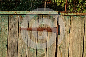 One old rusty metal brown door hinge on gray wooden fence