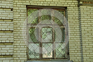 One old window behind an iron grate on a brown brick wall