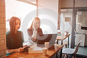 One-on-one meeting.Two young business women sitting at table in cafe. Girl shows colleague information on laptop screen