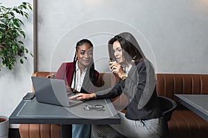 One-on-one meeting.Two young business women sitting at table in cafe. Girl shows colleague information on laptop screen. Girl