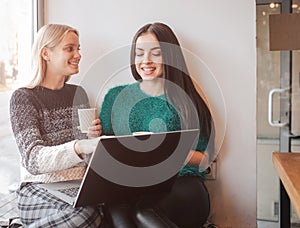 One-on-one meeting.Two young business women sitting at table in cafe. Girl shows colleague information on laptop screen